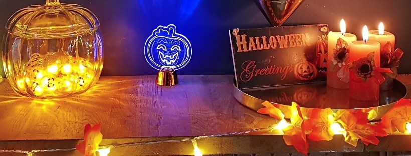 Halloween bar display with candles, orange maple leaf garland, neon blue pumpkin light, and glass pumpkin jar with orange lights inside.