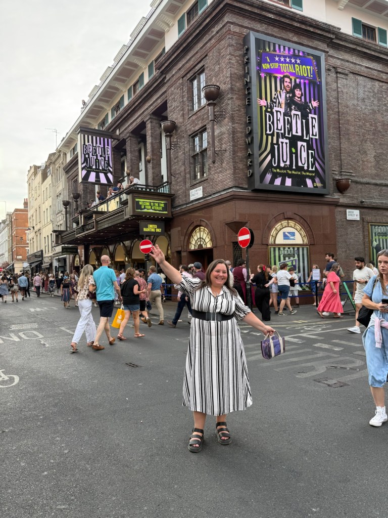 LOACM sees Beetlejuice the Musical. Woman standing in the middle of the road outside the London Theatre with Beetlejuice advertising.