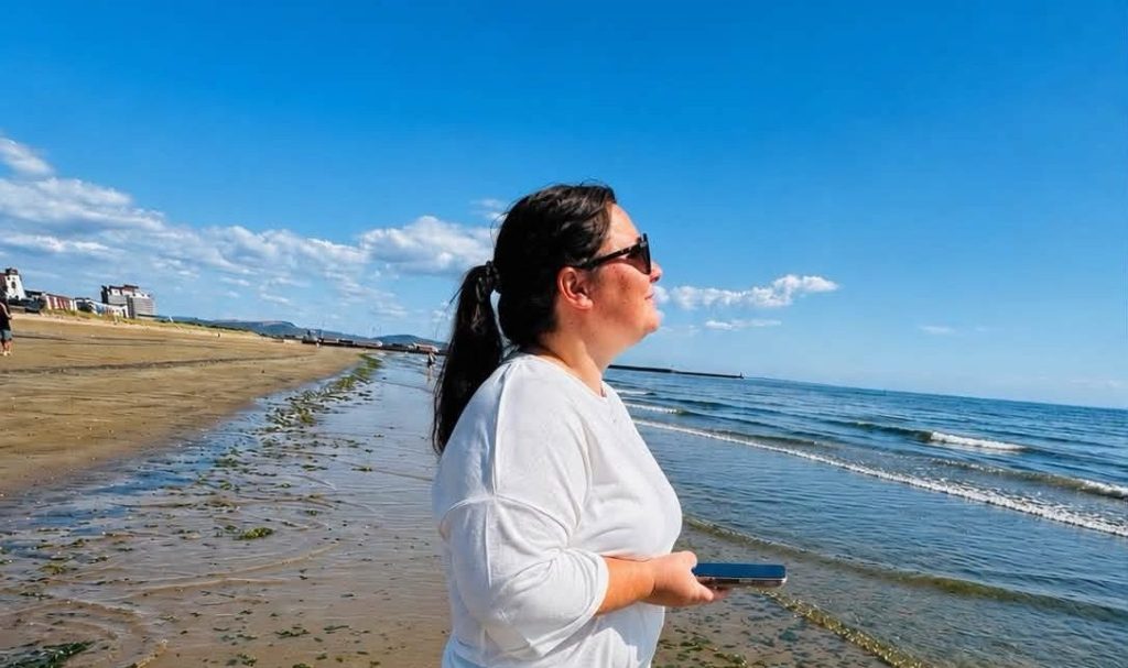 woman on a beach looking out over the sea with a blue sky.