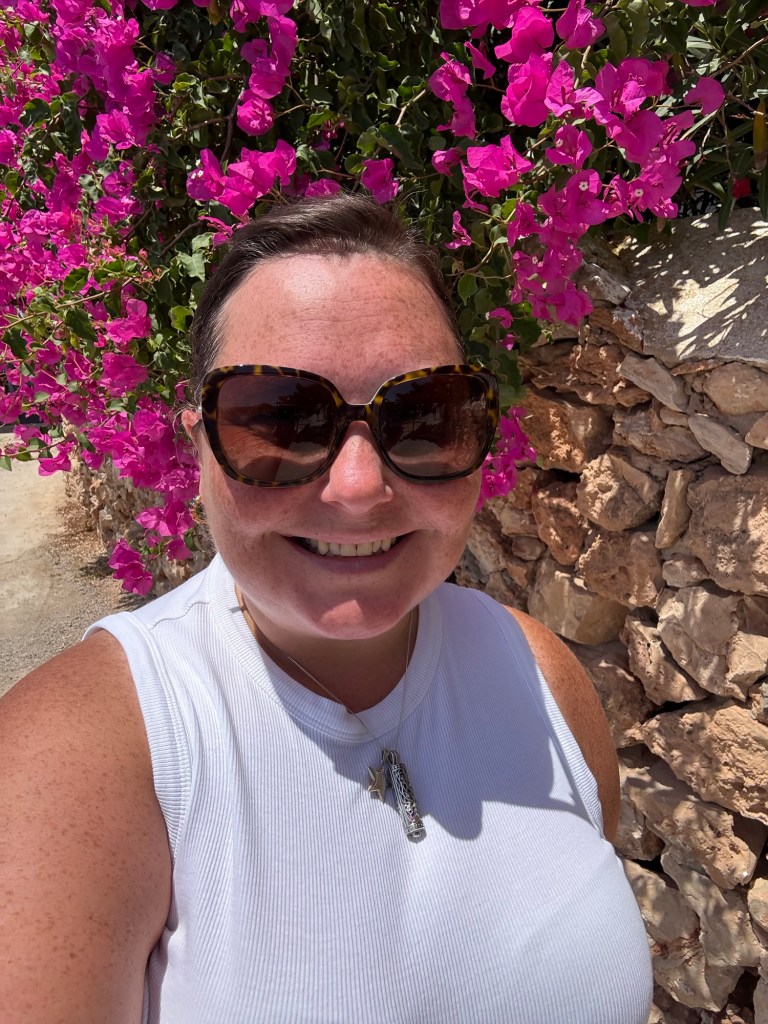 LOACM in San Antonio, Ibiza. Vibrant pink flowers hang over a stone wall in the background.
